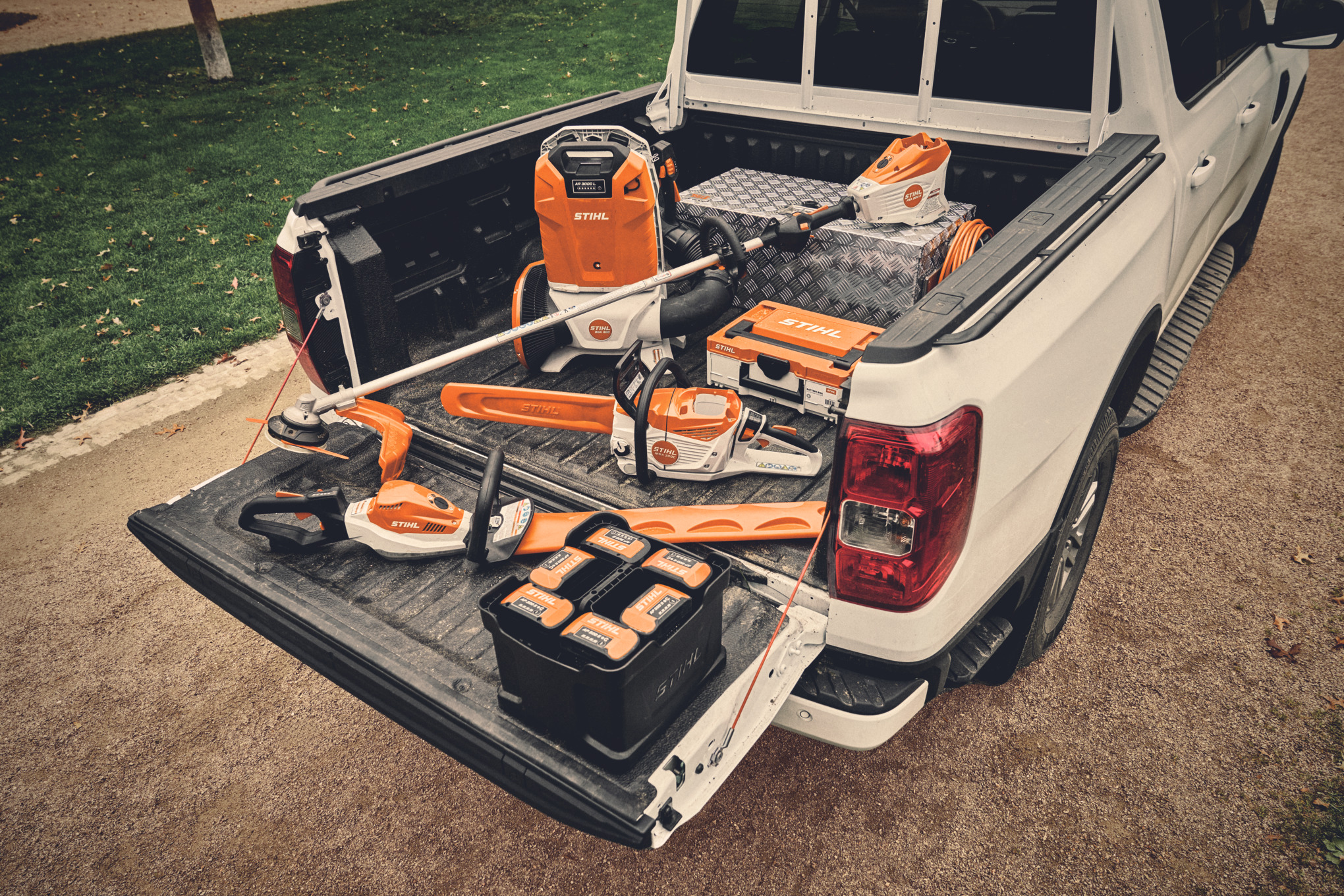Кілька акумуляторних пристроїв AP System від STIHL та відповідні акумулятори на зарядній поверхні автомобіля