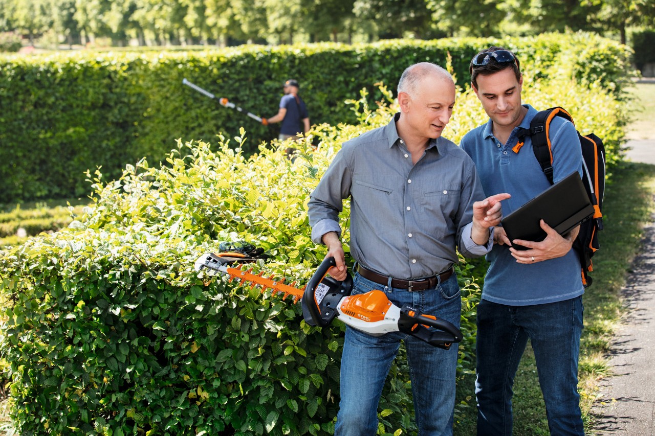 Доктор Ніколас Штіль тримає в руці кущоріз STIHL і розмовляє з людиною, яка стоїть поруч з ним і тримає в руках ноутбук.