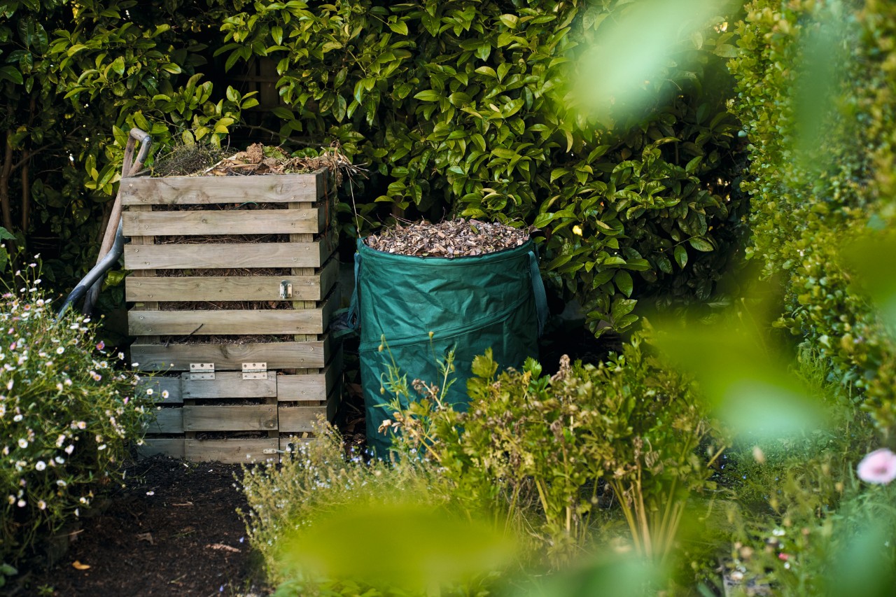Hölzerner Kompost, daneben ein Sack mit Laub im Garten