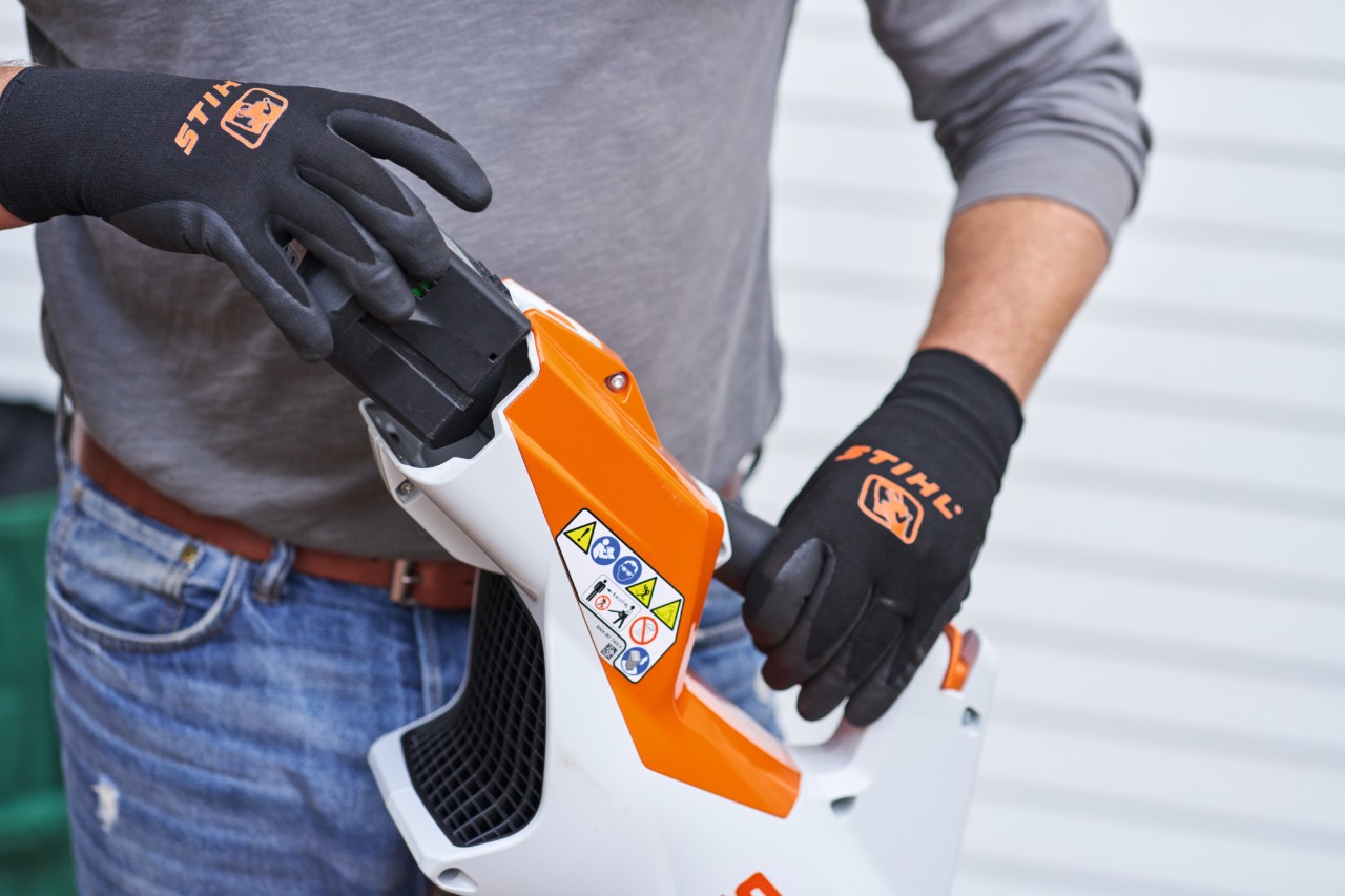Людина в чорних рукавичках STIHL виймає акумулятор з пневматичної рушниці