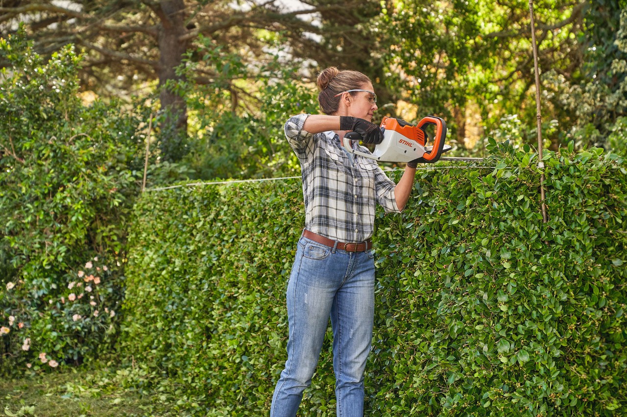 Eine Frau schneidet mit der STIHL Akku-Heckenschere HSA 45 eine Hecke in Form