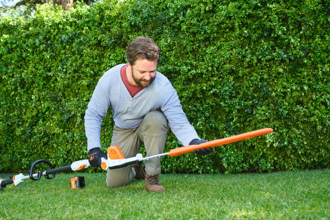 Чоловік перед живоплотом кладе акумуляторний кущоріз STIHL HLA 56 на газон