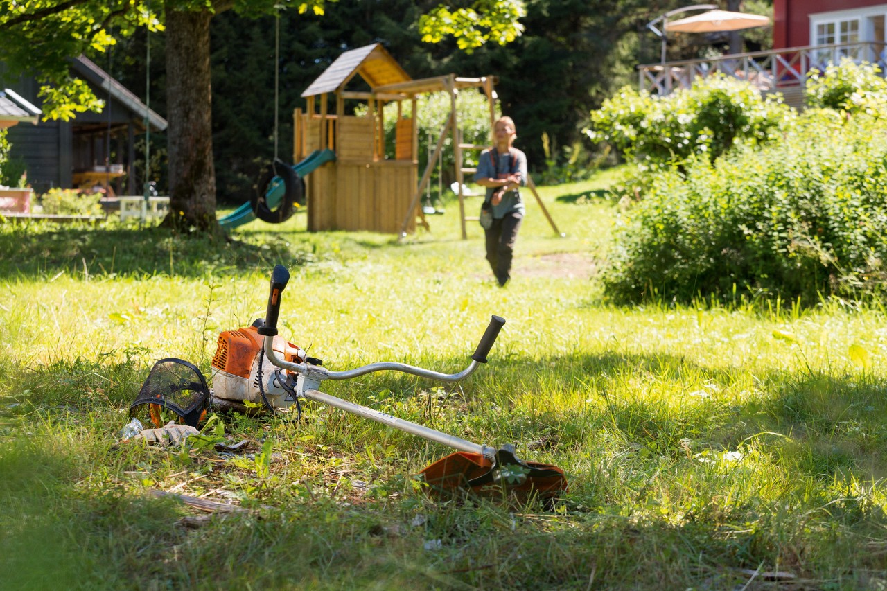 Мотокоса STIHL FS 240 лежить у траві, на задньому плані чоловік готується до обслуговування