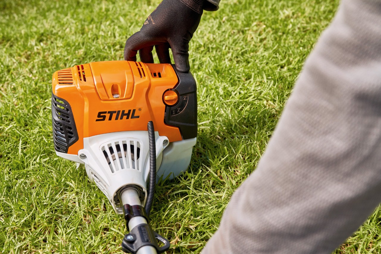 Чоловік щільно притискає бензинову мотокосу STIHL FS 91 до землі
