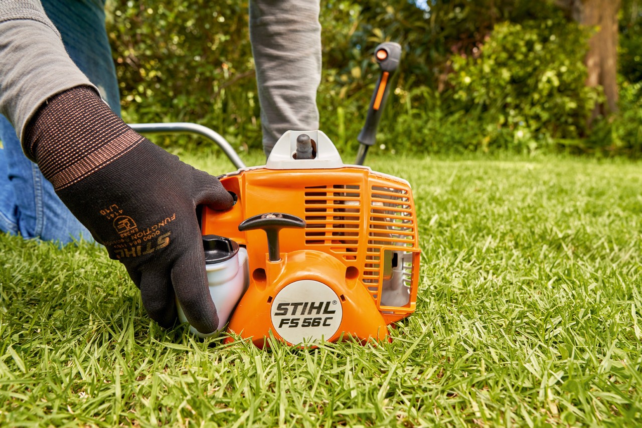 Чоловік натискає на паливний насос бензинової мотокоси STIHL FS 56, щоб запустити мотокосу