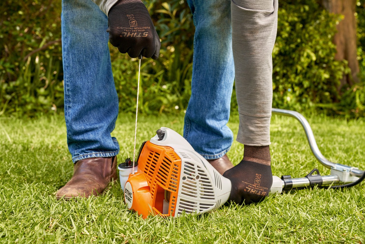 Чоловік тягне за мотузку стартера бензинової мотокоси STIHL FS 56