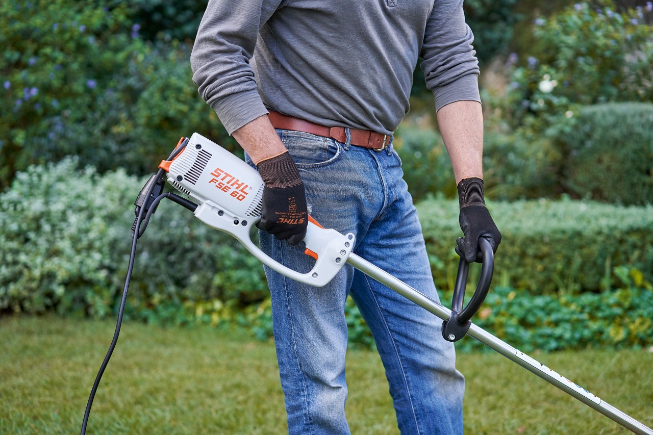 Чоловік у захисних рукавичках тримає електричну мотокосу STIHL FSE 60 обома руками