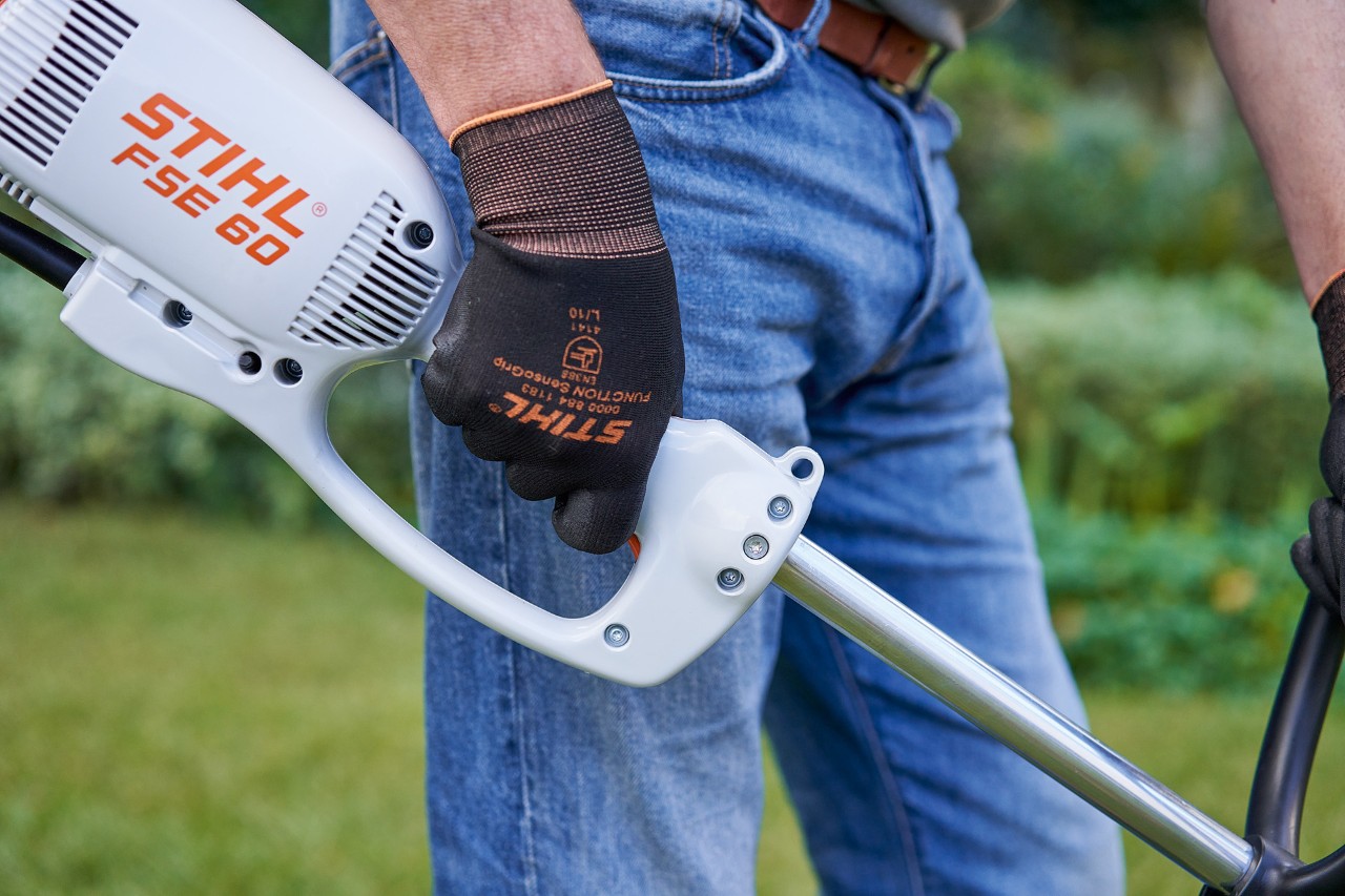 Чоловік натискає вимикач на ручці керування електричної мотокоси STIHL FSE 60