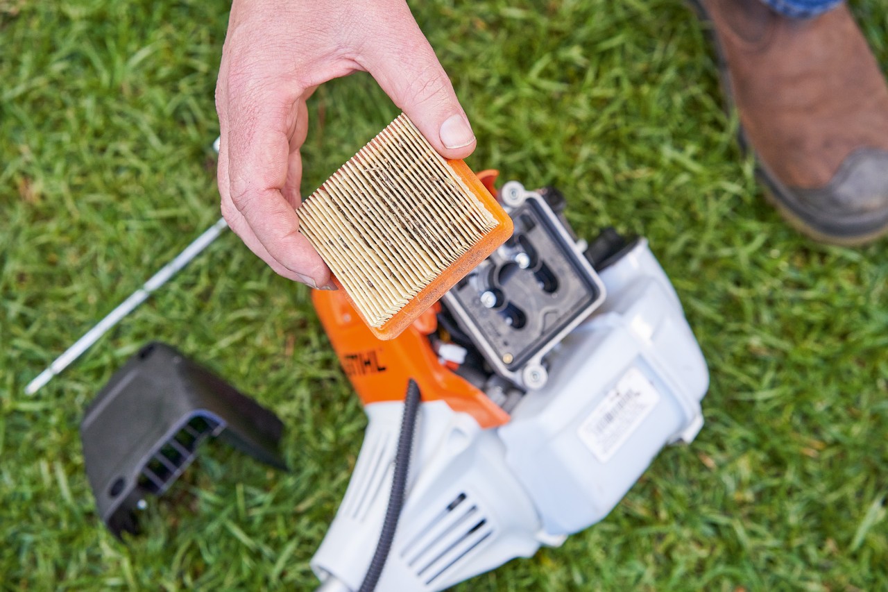 Людина знімає повітряний фільтр мотокоси STIHL, щоб почистити його.