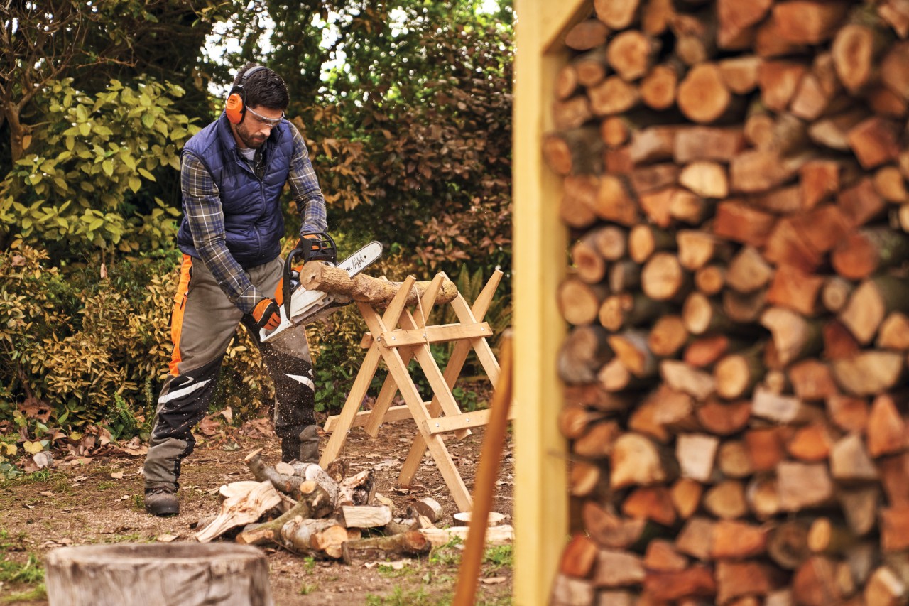 Чоловік у захисному спорядженні розпилює поліно для складування у дров’янику