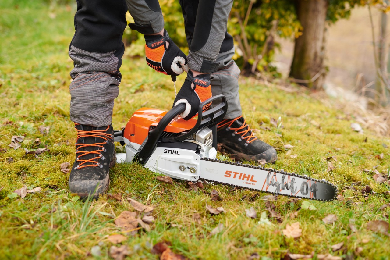Мотопилу STIHL MS261CM покладено на землю в лісі, людина її безпечно запустила.