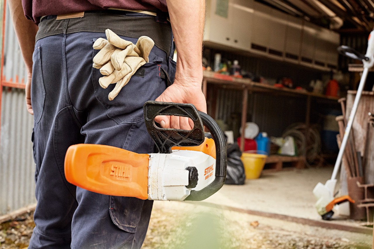 Чоловік стоїть біля майстерні з акумуляторною ланцюговою пилкою STIHL з захистом шини