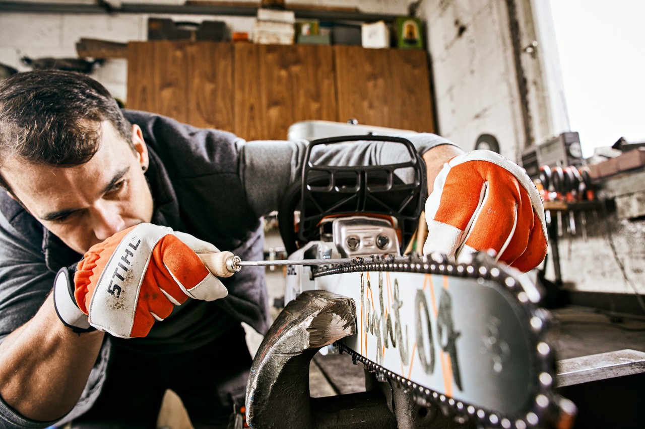 Чоловік у рукавичках STIHL підпилює ланцюг бензинової бензопили STIHL 261 C-M круглим напилком