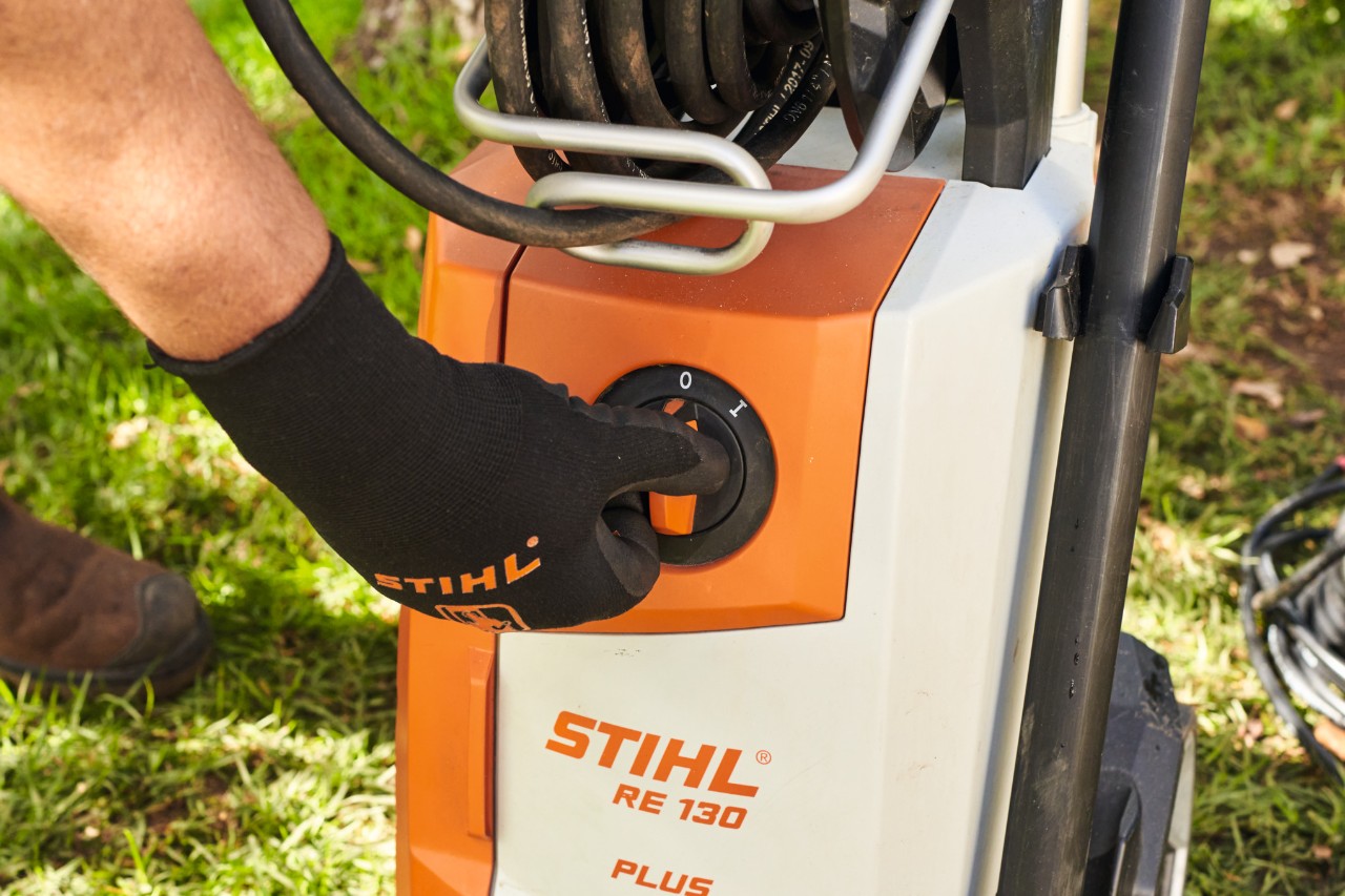 Nahaufnahme, wie jemand mit schwarzen Schutzhandschuhen den Hochdruckreiniger STIHL RE 130 ausschaltet