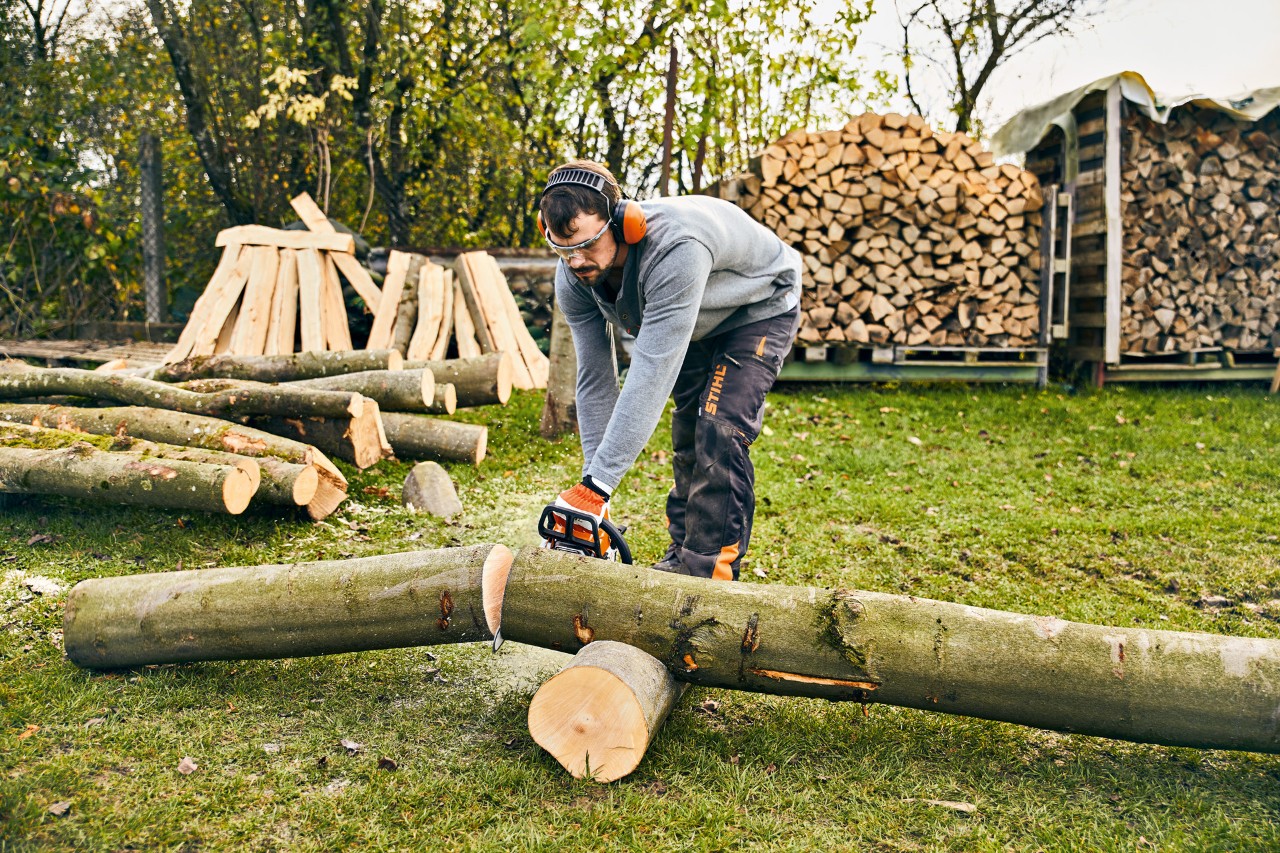 Mann möchte Pflanztrog selber bauen und zersägt dazu einen Baumstamm mit der STIHL Benzin-Motorsäge MS 180