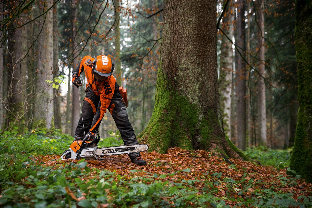 Чоловік у захисному одязі запускає бензопилу STIHL MS 500i на землі в листяному лісі