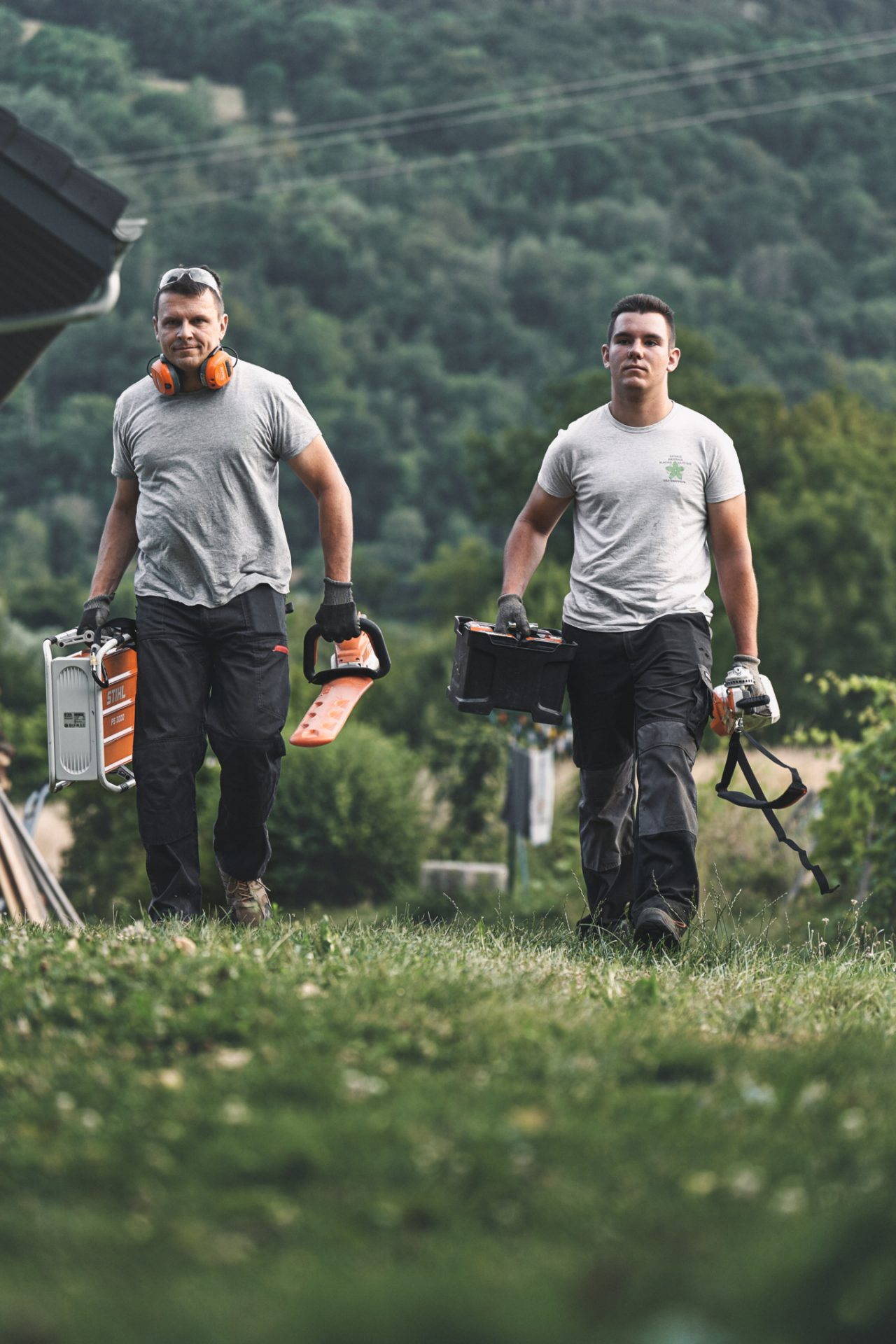 Двоє фахівців йдуть лугом з акумуляторними пристроями STIHL