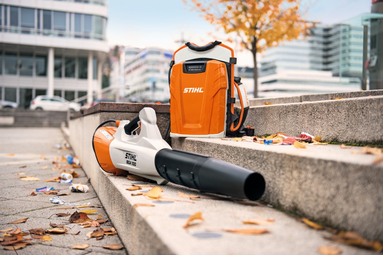 Акумуляторний повітродувний пристрій STIHL BGA 100 і професійний ранцевий акумулятор STIHL AR 3000 L лежать на кам’яних сходах з листям