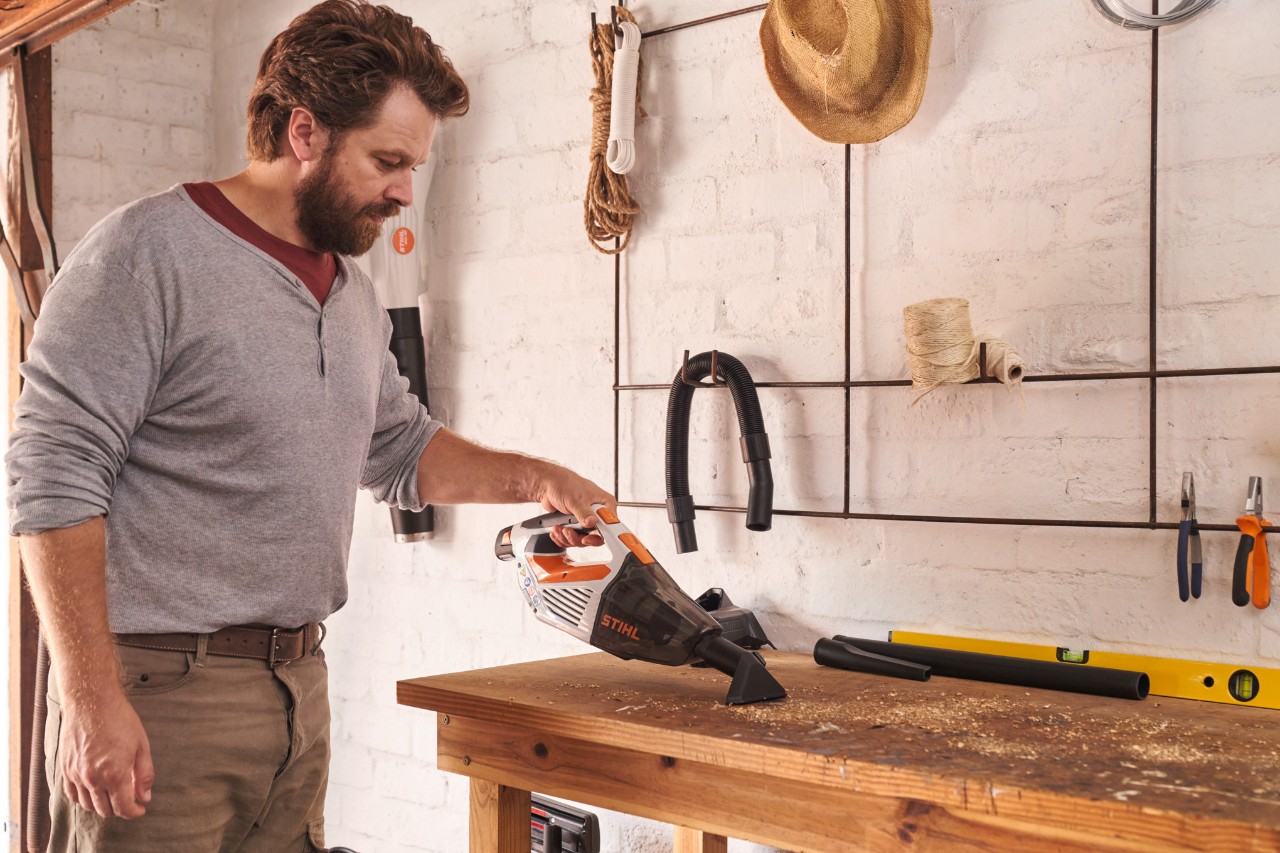 Чоловік пилососить верстак за допомогою акумуляторного ручного пилососа STIHL SEA 20
