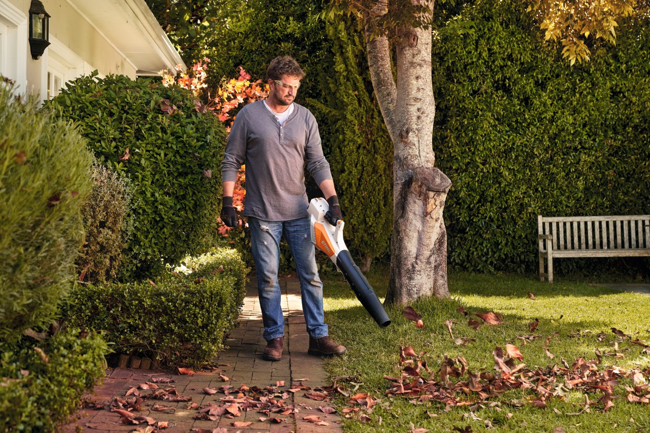 Чоловік здуває листя з газону акумуляторним повітродувним пристроєм STIHL BGA 57