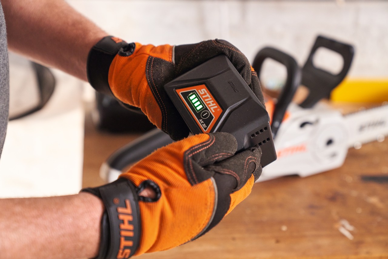 Людина в захисних рукавичках STIHL тримає в руках літій-іонний акумулятор STIHL