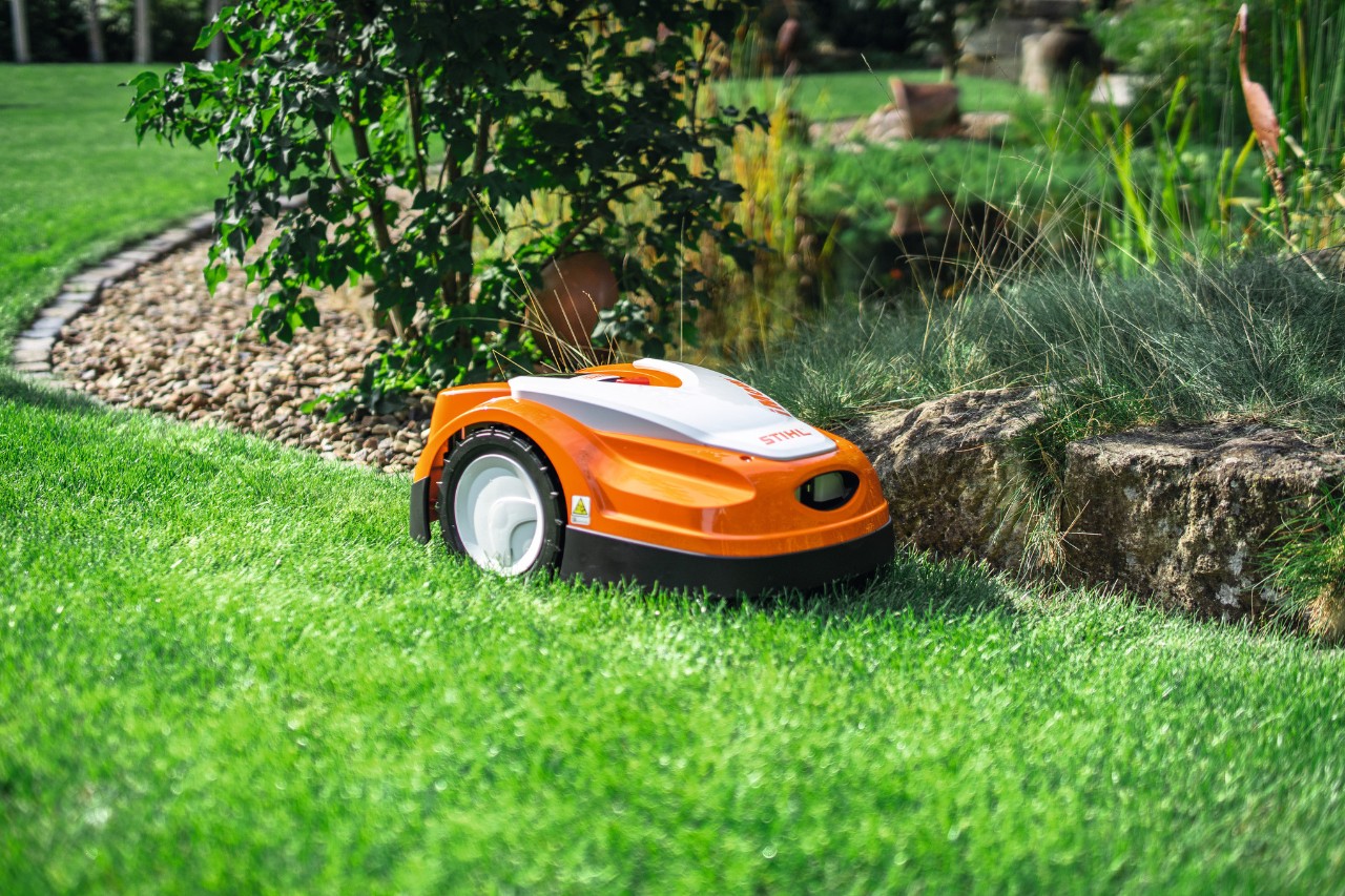 STIHL iMOW RMI 422 косить газон у саду біля невеликої кам’яної стіни.