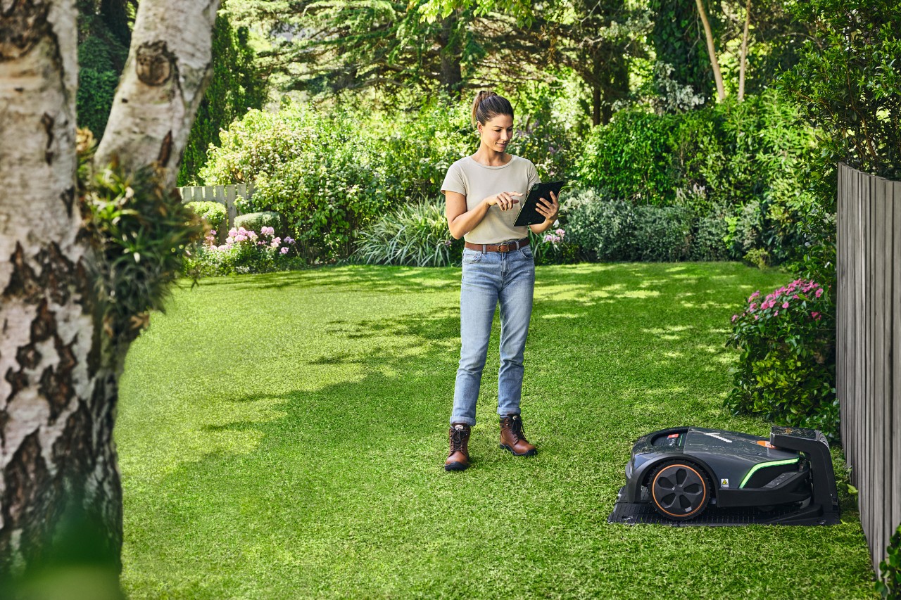 Жінка керує STIHL iMOW® EVO за допомогою планшета у своєму саду